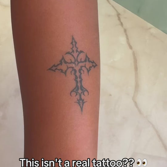 Close-up of an artist-designed temporary cross tattoo showing realistic skin movement, natural blue-black ink color, and a real tattoo look.