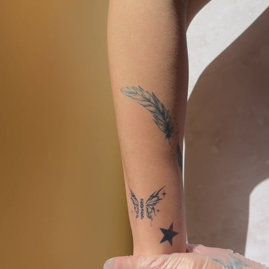 Twin Feathers fine line temporary tattoo applied on the inner forearm, showing a realistic black ink look.