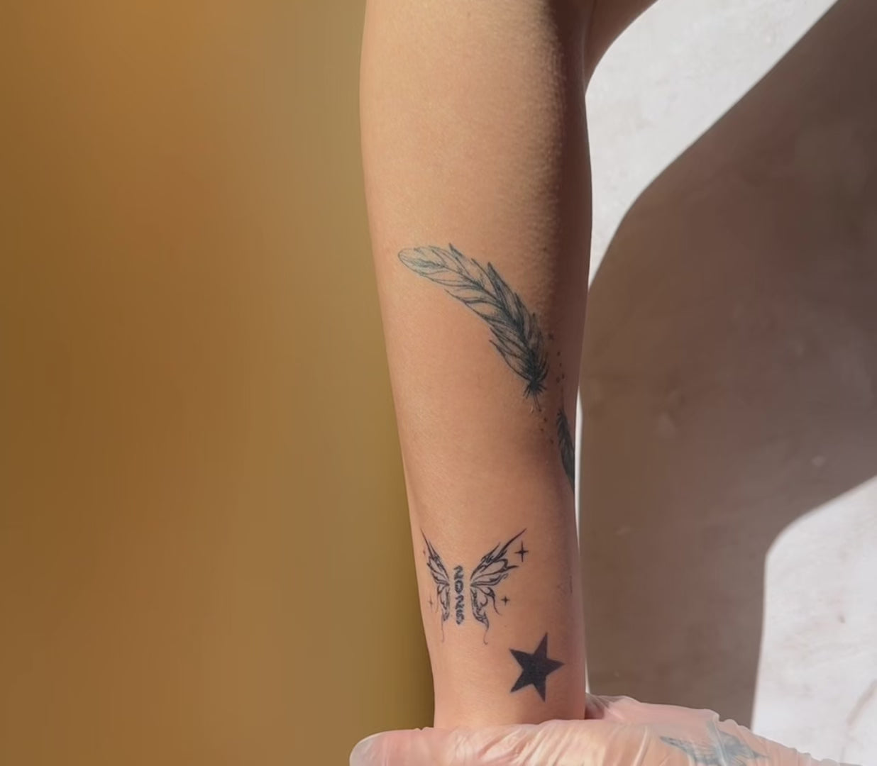 Twin Feathers fine line temporary tattoo applied on the inner forearm, showing a realistic black ink look.